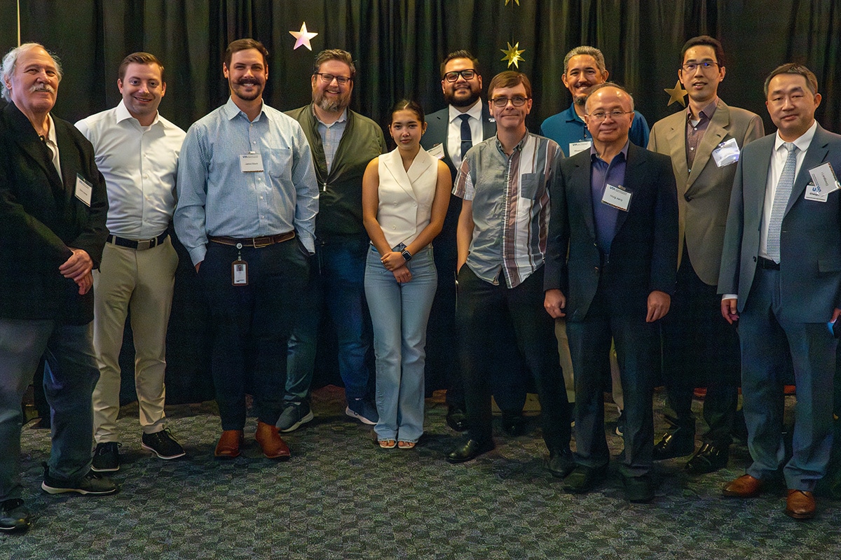 Twelve people standing in front of a black curtain with star decorations, dressed in business casual attire - opens in a new tab