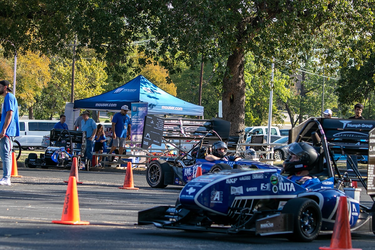 People driving racecars past a Mouser tent - opens in a new tab